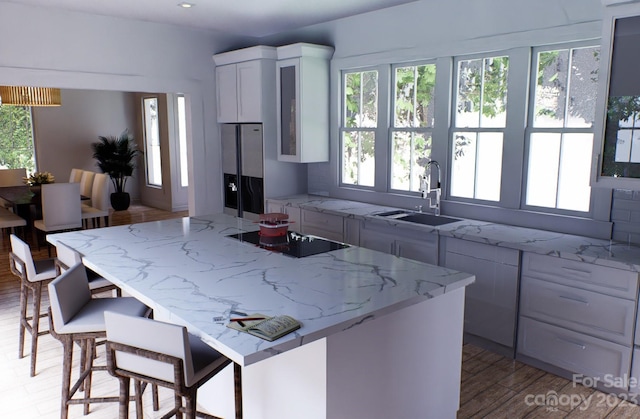 kitchen featuring light stone countertops, white cabinetry, black electric stovetop, and sink