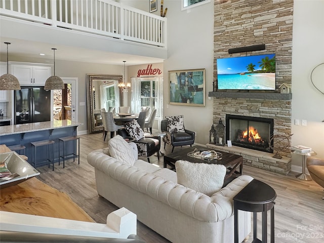 living room featuring a stone fireplace, a chandelier, a towering ceiling, and light hardwood / wood-style flooring