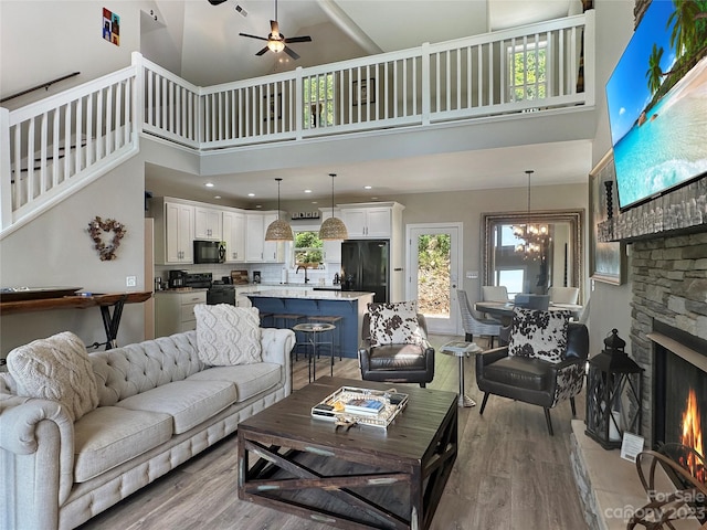 living room featuring light hardwood / wood-style flooring, plenty of natural light, a high ceiling, and a stone fireplace