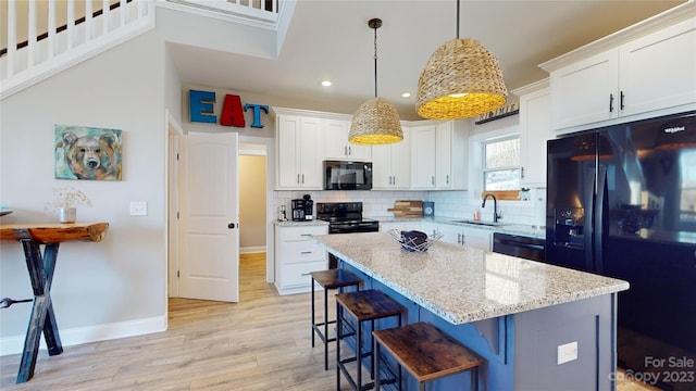 kitchen featuring a kitchen breakfast bar, decorative light fixtures, black appliances, backsplash, and sink