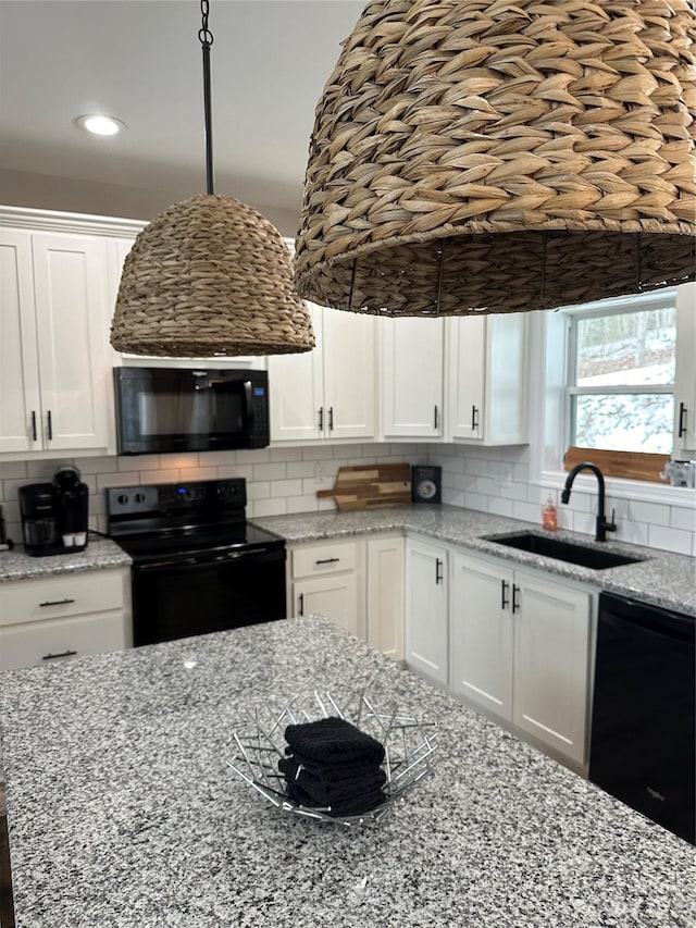 kitchen with light stone counters, white cabinetry, black appliances, backsplash, and sink