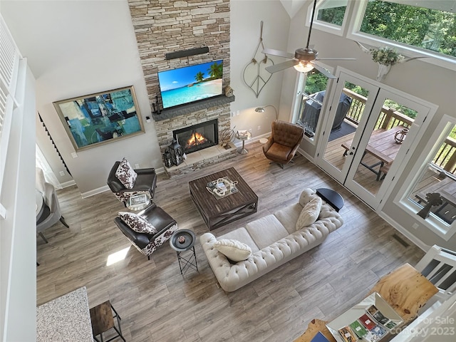 living room featuring ceiling fan, a fireplace, light wood-type flooring, and a towering ceiling