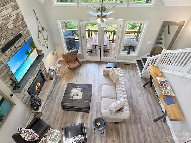 living room featuring french doors, ceiling fan, light hardwood / wood-style flooring, a high ceiling, and a stone fireplace