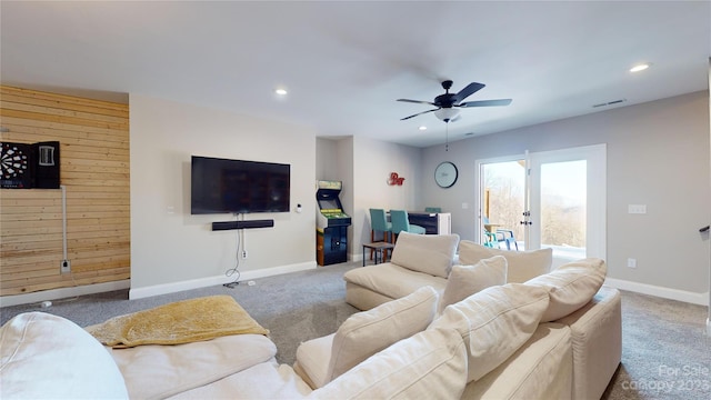 carpeted living room with ceiling fan, wood walls, and french doors