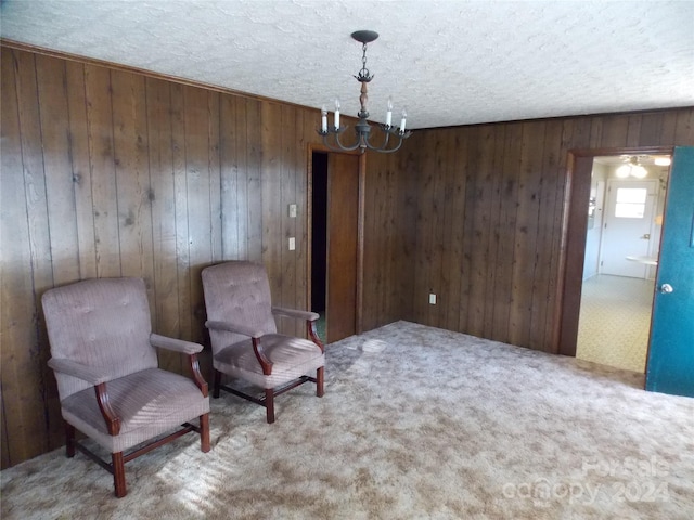 living area featuring a textured ceiling, wood walls, carpet flooring, and an inviting chandelier