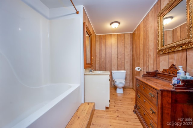 full bathroom featuring toilet, wood-type flooring, tub / shower combination, vanity, and wooden walls