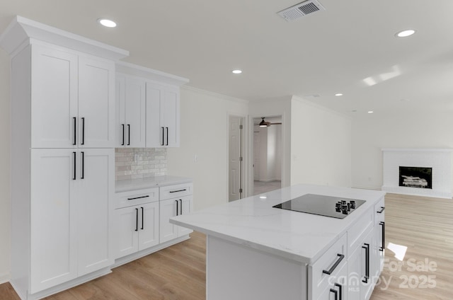 kitchen featuring light hardwood / wood-style flooring, backsplash, light stone counters, black electric stovetop, and white cabinets