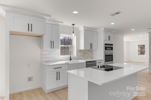 kitchen featuring pendant lighting, a kitchen island, white cabinets, and appliances with stainless steel finishes