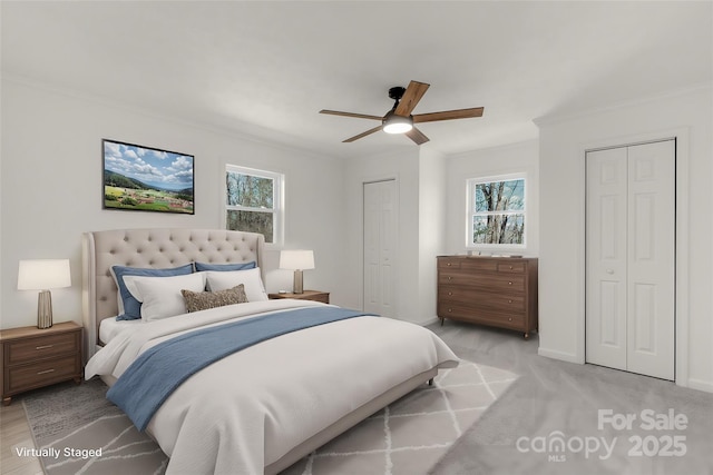 bedroom featuring crown molding, two closets, light colored carpet, and ceiling fan