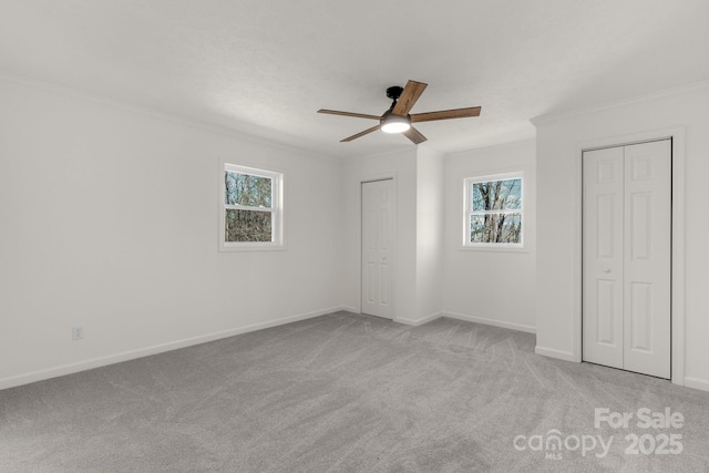 unfurnished bedroom with light carpet, ceiling fan, crown molding, and multiple closets