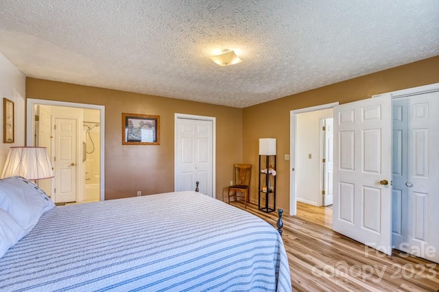 bedroom featuring light hardwood / wood-style flooring, connected bathroom, two closets, and a textured ceiling