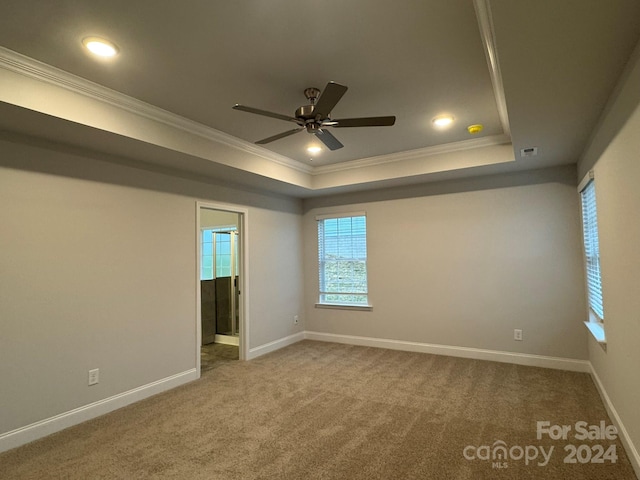 empty room featuring a raised ceiling, ceiling fan, carpet floors, and ornamental molding