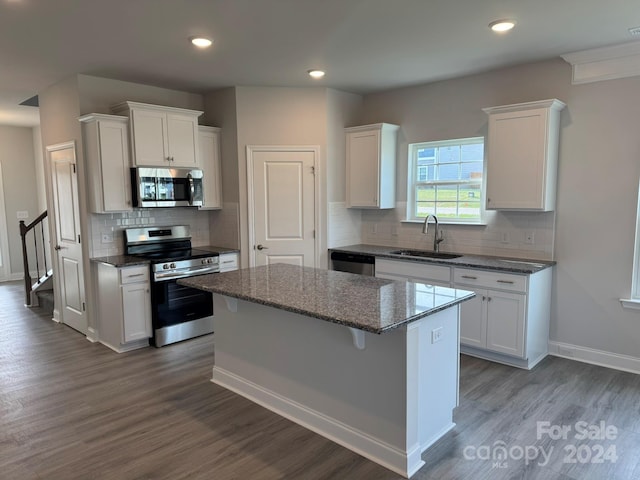 kitchen with stainless steel appliances, sink, stone countertops, white cabinets, and a kitchen island