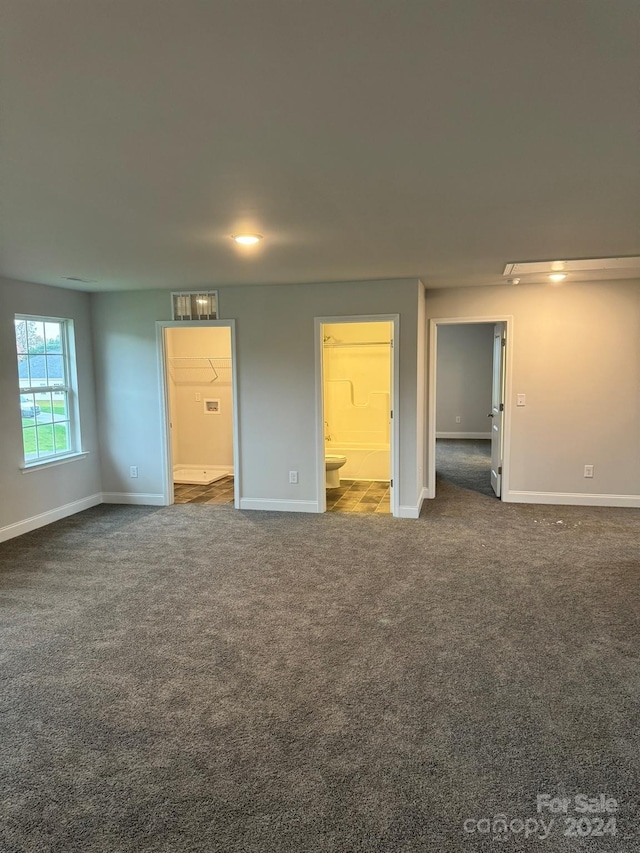 unfurnished bedroom featuring ensuite bath and dark carpet