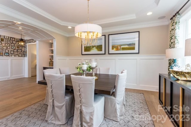 dining room featuring ornamental molding, a notable chandelier, a raised ceiling, and light wood-type flooring