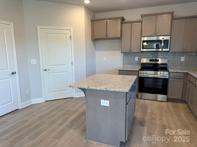 kitchen with light stone countertops, stainless steel appliances, backsplash, light hardwood / wood-style floors, and a kitchen island