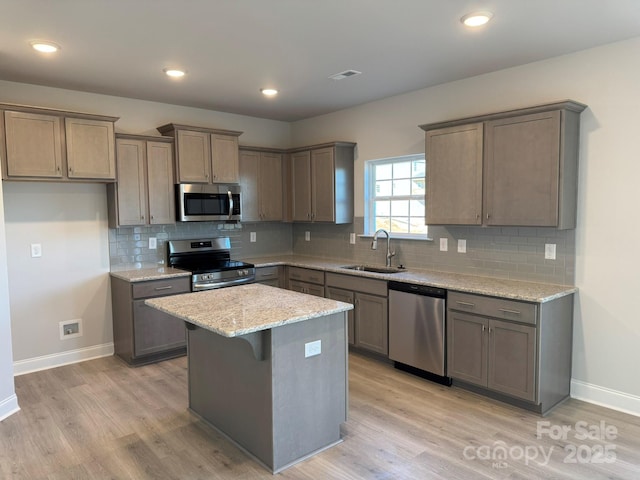 kitchen featuring a center island, sink, light hardwood / wood-style flooring, light stone countertops, and appliances with stainless steel finishes