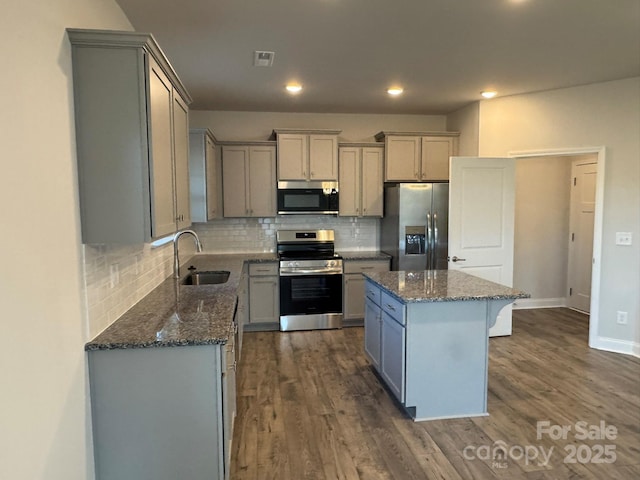 kitchen with dark stone counters, sink, appliances with stainless steel finishes, tasteful backsplash, and a kitchen island