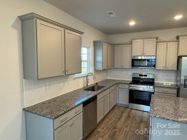 kitchen featuring sink, dark hardwood / wood-style floors, dark stone countertops, gray cabinets, and appliances with stainless steel finishes