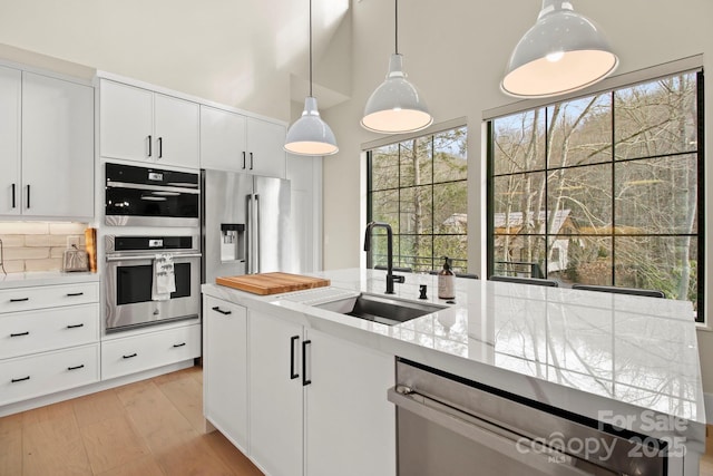 kitchen featuring pendant lighting, white cabinetry, stainless steel appliances, tasteful backsplash, and sink