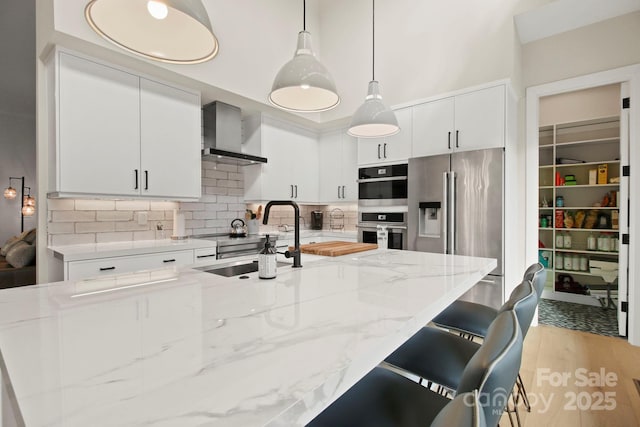 kitchen featuring decorative light fixtures, white cabinets, and wall chimney exhaust hood