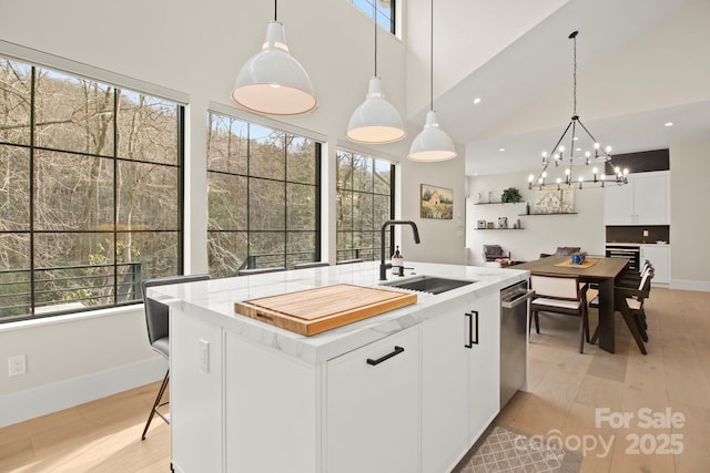 kitchen with sink, hanging light fixtures, white cabinets, and a center island with sink