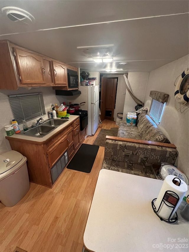 kitchen with light hardwood / wood-style floors, white fridge, sink, and black microwave