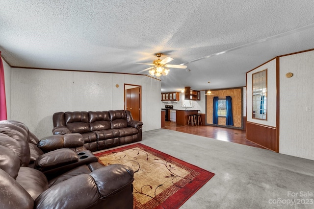 living room featuring a textured ceiling, ceiling fan, carpet floors, and ornamental molding