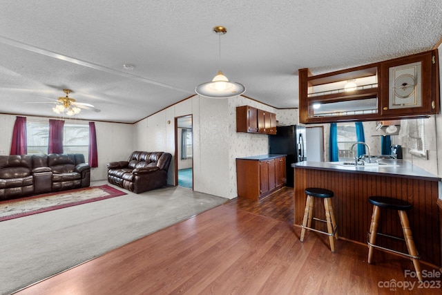 interior space with dark colored carpet, ceiling fan, a kitchen bar, a textured ceiling, and kitchen peninsula