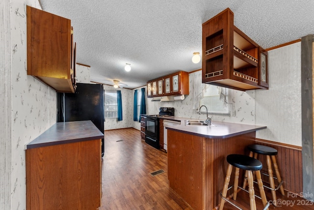 kitchen with a breakfast bar area, dark hardwood / wood-style floors, black electric range, a textured ceiling, and sink