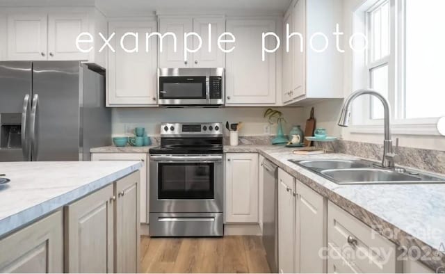 kitchen featuring appliances with stainless steel finishes, white cabinets, light hardwood / wood-style flooring, light stone countertops, and sink