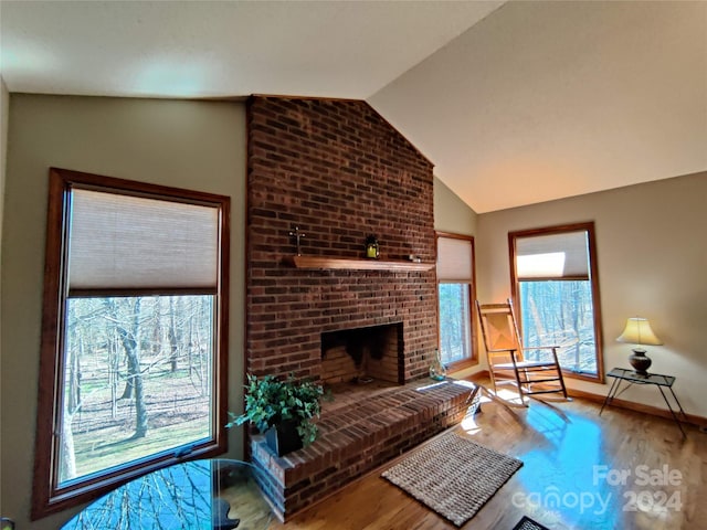 living room with brick wall, hardwood / wood-style floors, a brick fireplace, and vaulted ceiling