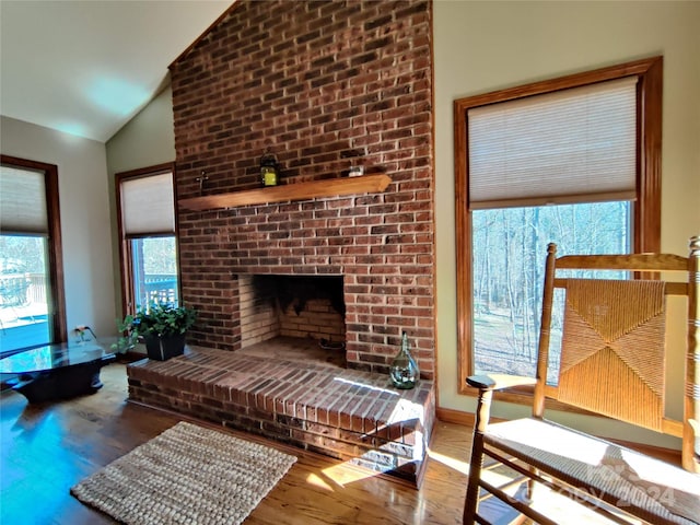 living room with brick wall, a fireplace, hardwood / wood-style flooring, and lofted ceiling