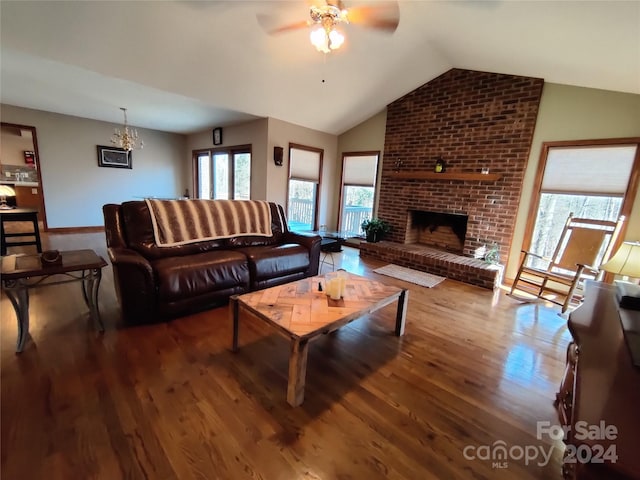 living room featuring a fireplace, ceiling fan with notable chandelier, hardwood / wood-style floors, brick wall, and lofted ceiling