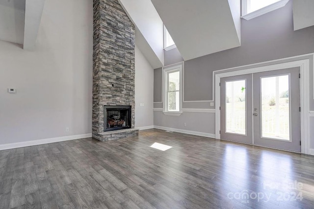 unfurnished living room featuring dark hardwood / wood-style floors, french doors, a high ceiling, and a stone fireplace