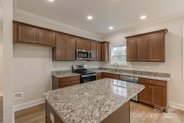 kitchen with sink, light hardwood / wood-style flooring, appliances with stainless steel finishes, a kitchen island, and light stone counters