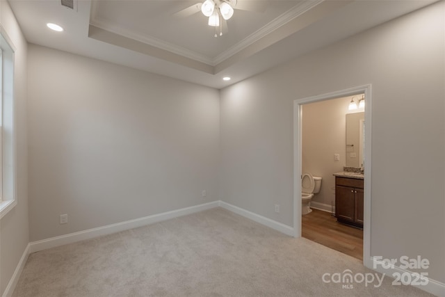 unfurnished bedroom featuring connected bathroom, ceiling fan, a raised ceiling, crown molding, and light colored carpet