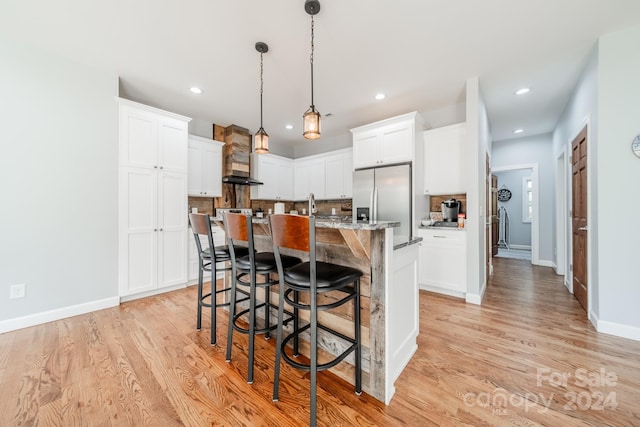 kitchen with an island with sink, white cabinetry, light hardwood / wood-style floors, and pendant lighting