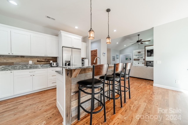 kitchen with ceiling fan, stainless steel fridge with ice dispenser, hanging light fixtures, light hardwood / wood-style flooring, and a breakfast bar area