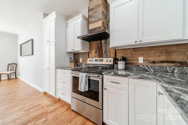 kitchen with dark stone counters, stainless steel range with electric stovetop, white cabinets, light hardwood / wood-style flooring, and wall chimney exhaust hood