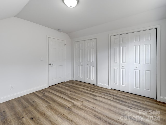 unfurnished bedroom with vaulted ceiling, light wood-type flooring, and two closets