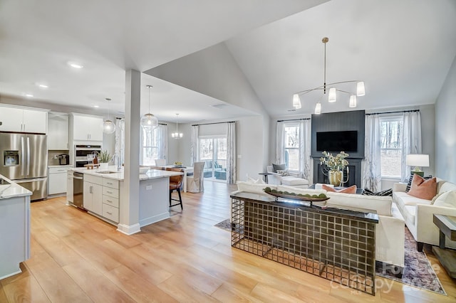 living room with sink, a chandelier, vaulted ceiling, and light hardwood / wood-style floors