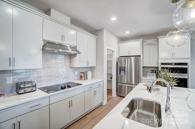 kitchen featuring white cabinetry, stainless steel appliances, light wood-type flooring, backsplash, and hanging light fixtures