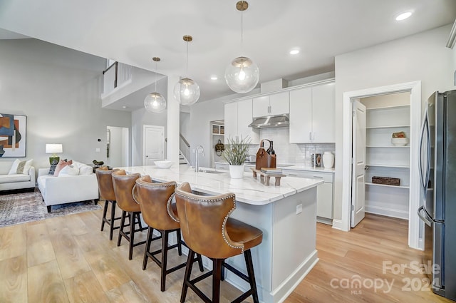 kitchen with tasteful backsplash, stainless steel fridge, light hardwood / wood-style floors, white cabinetry, and a kitchen island with sink