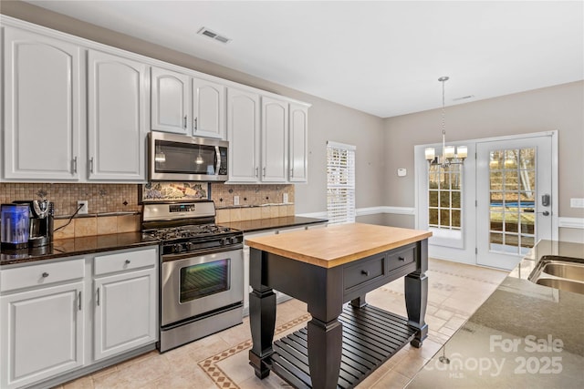 kitchen featuring backsplash, stainless steel appliances, hanging light fixtures, and white cabinets