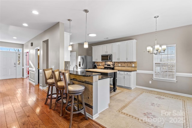 kitchen with appliances with stainless steel finishes, a breakfast bar, white cabinets, decorative backsplash, and hanging light fixtures