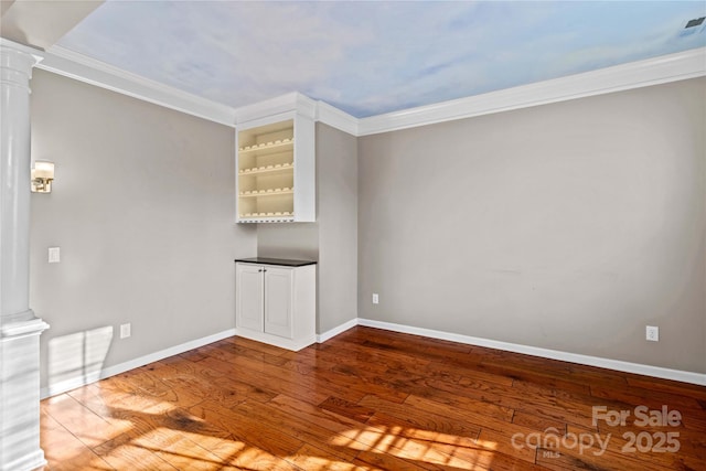 spare room with ornate columns, wood-type flooring, built in features, and crown molding