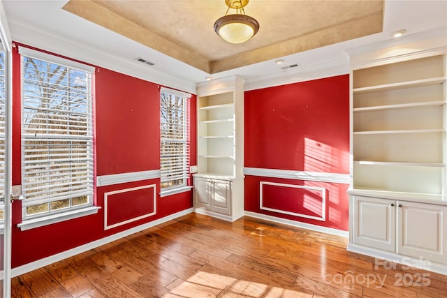 interior space with wood-type flooring, built in shelves, and a tray ceiling