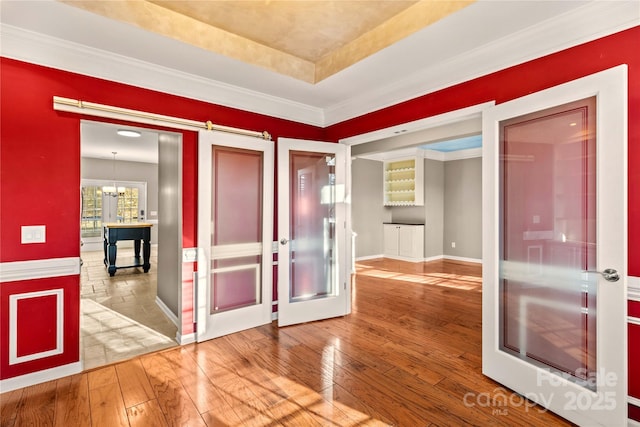 interior space featuring hardwood / wood-style flooring, a barn door, french doors, a raised ceiling, and a chandelier