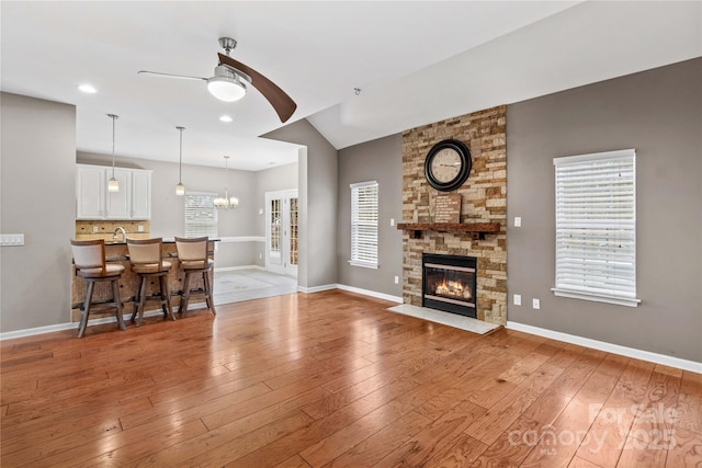 living room featuring lofted ceiling, a stone fireplace, light hardwood / wood-style flooring, and ceiling fan